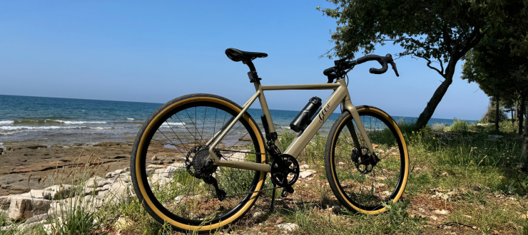 Ein Geero Gravel E-Bike in Armee-Grün steht auf einem felsigen Hügel. Im Hintergrund sieht man das Meer.